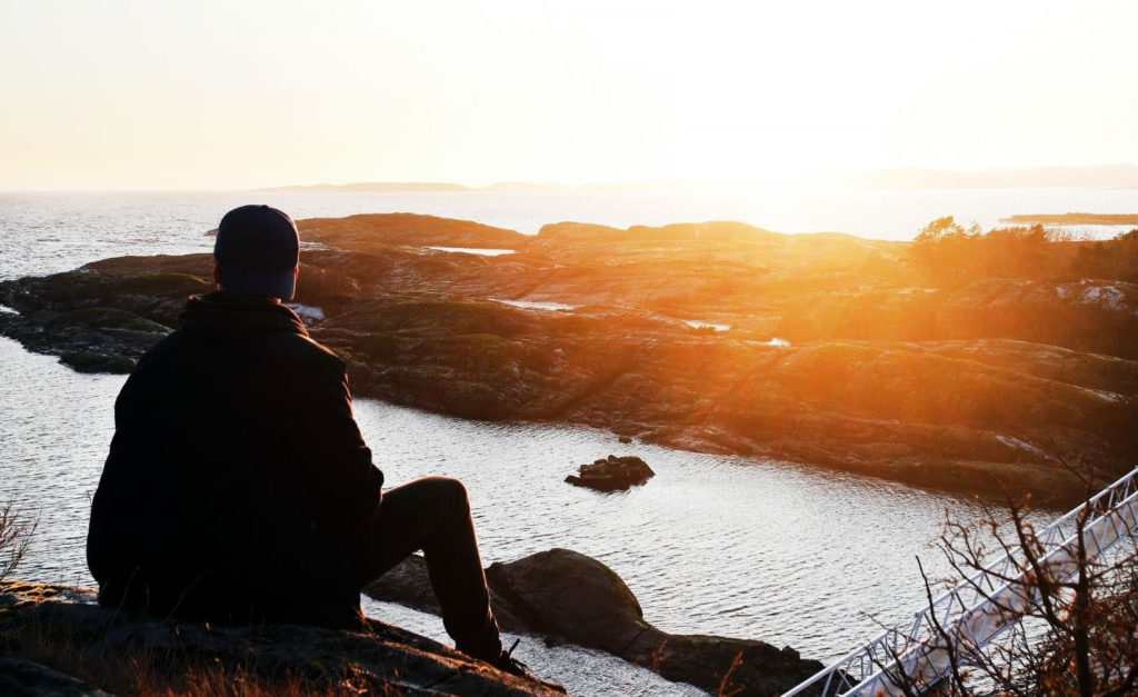 person looking over the edge of a cliff into a sunset