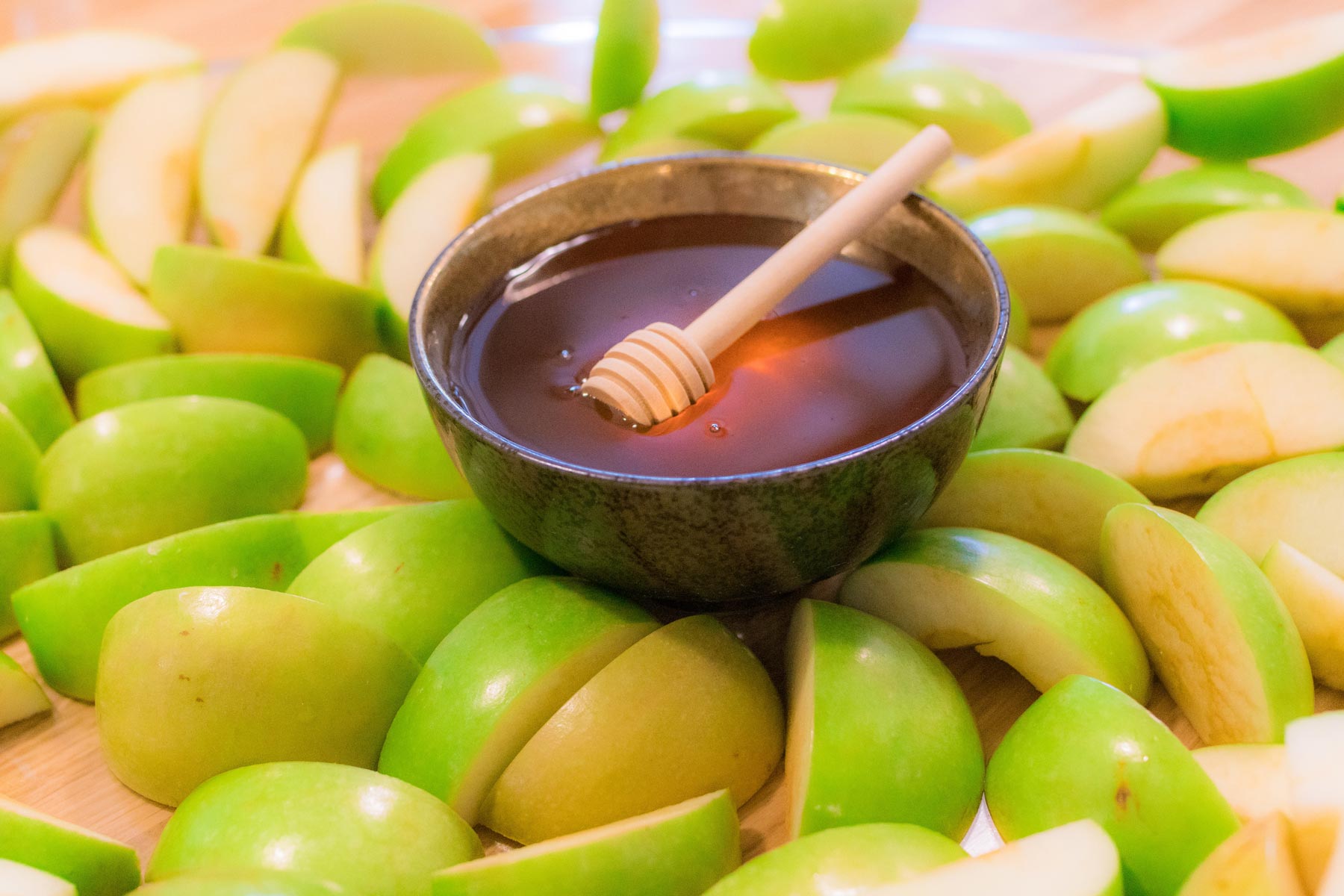 lots of green apple slices surrounding a bowl of honey