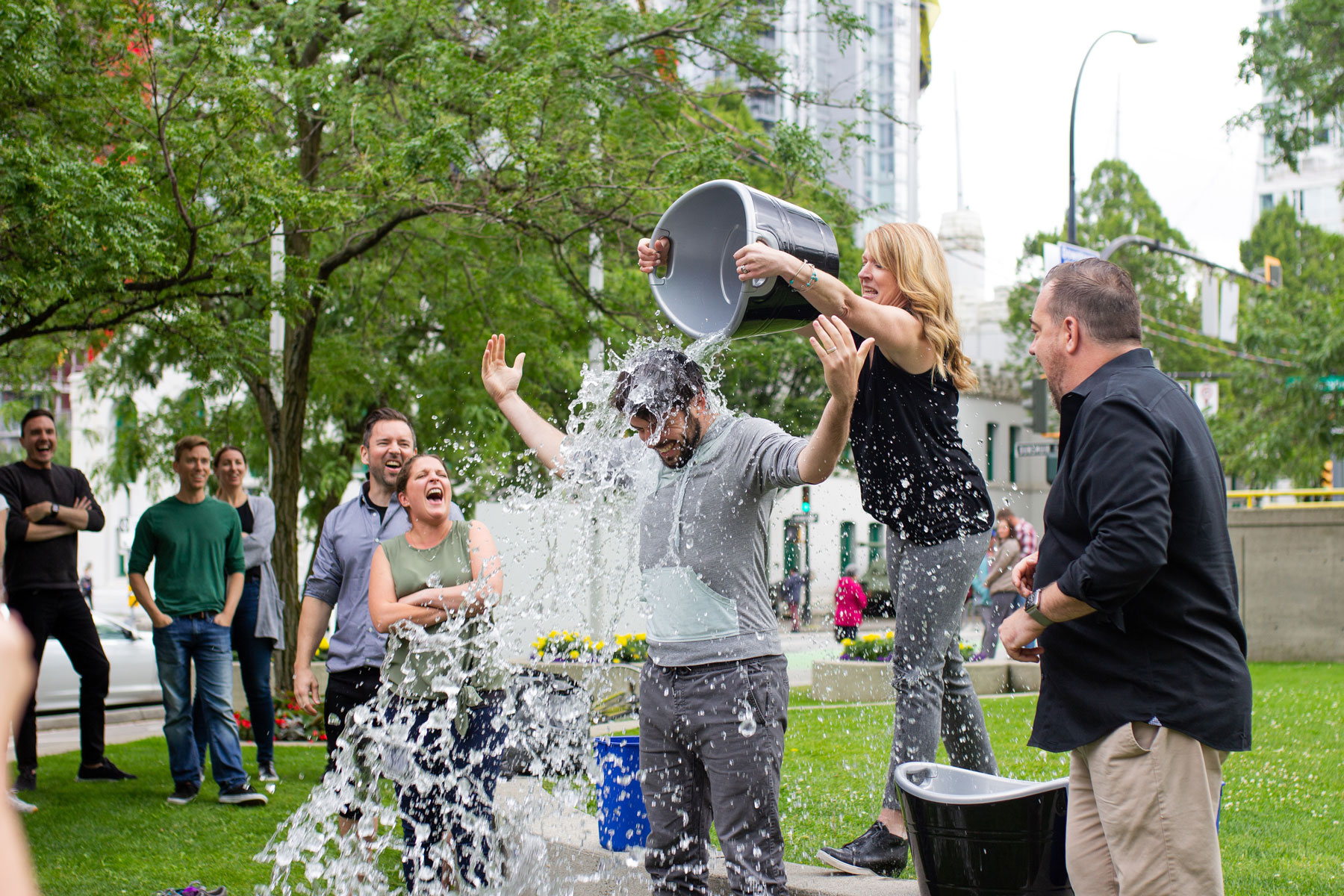 a lady pouring a bucket of water on a man's head while a crowd is watching