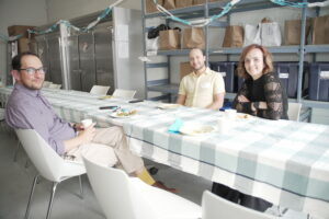 Three people sitting at a long table, smiling into the camera.