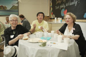 Three people sitting at a table and smiling into the camera while eating.
