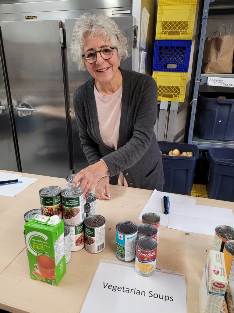 A smiling volunteer sorts vegetarian soups at a table in the JFS warehouse.