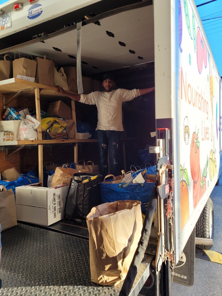 Staff member Sammy stands inside the JFS deliver truck surrounded by bags of donated food.
