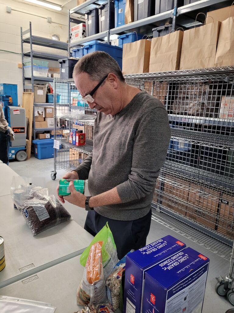 A volunteer with short hair and glasses checks an item of donated food for best before date and to determine if it it Kosher or not.