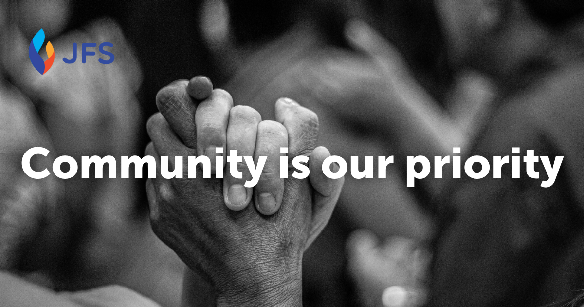 Text reads: community is our priority. Background image is black and white with two hands clasped in the forground and blurred people in the background.