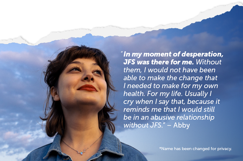 Person with dark, shoulder length hair and red lipstick smiles into the distance past the camera. A cloudy blue sunrise is behind them. Overlay text reads: “In my moment of desperation, JFS was there for me. Without them, I would not have been able to make the change that I needed to make for my own health. For my life. Usually I cry when I say that, because it reminds me that I would still be in an abusive relationship without JFS.” – Abby