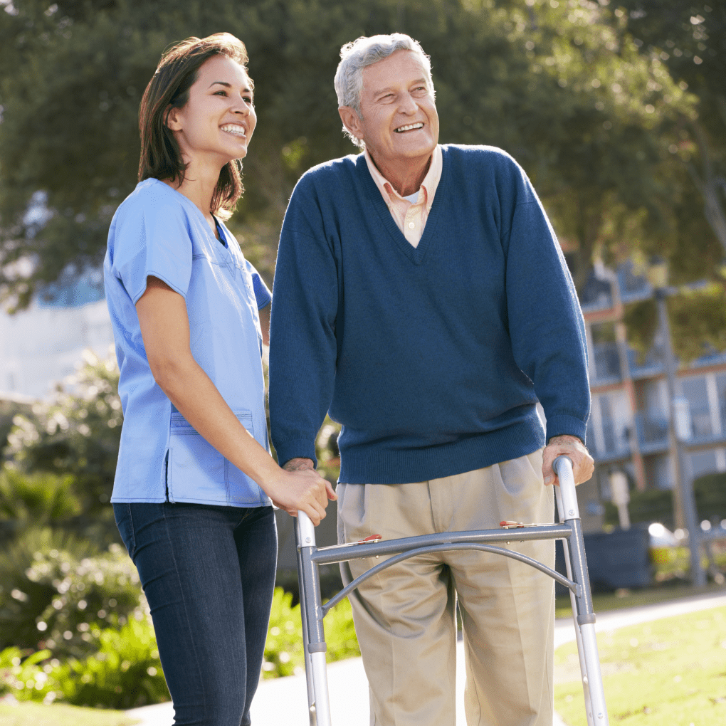 older man using walker stands outside with a smiling home support worker